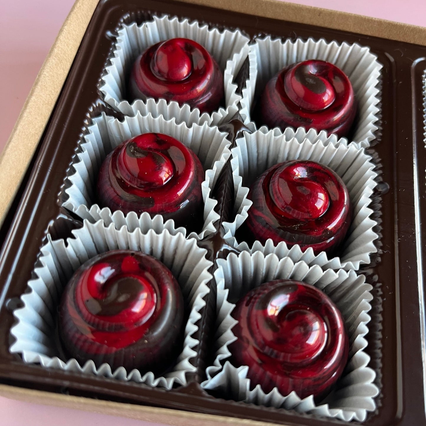 Box of red chocolates in white paper cups on a pink background