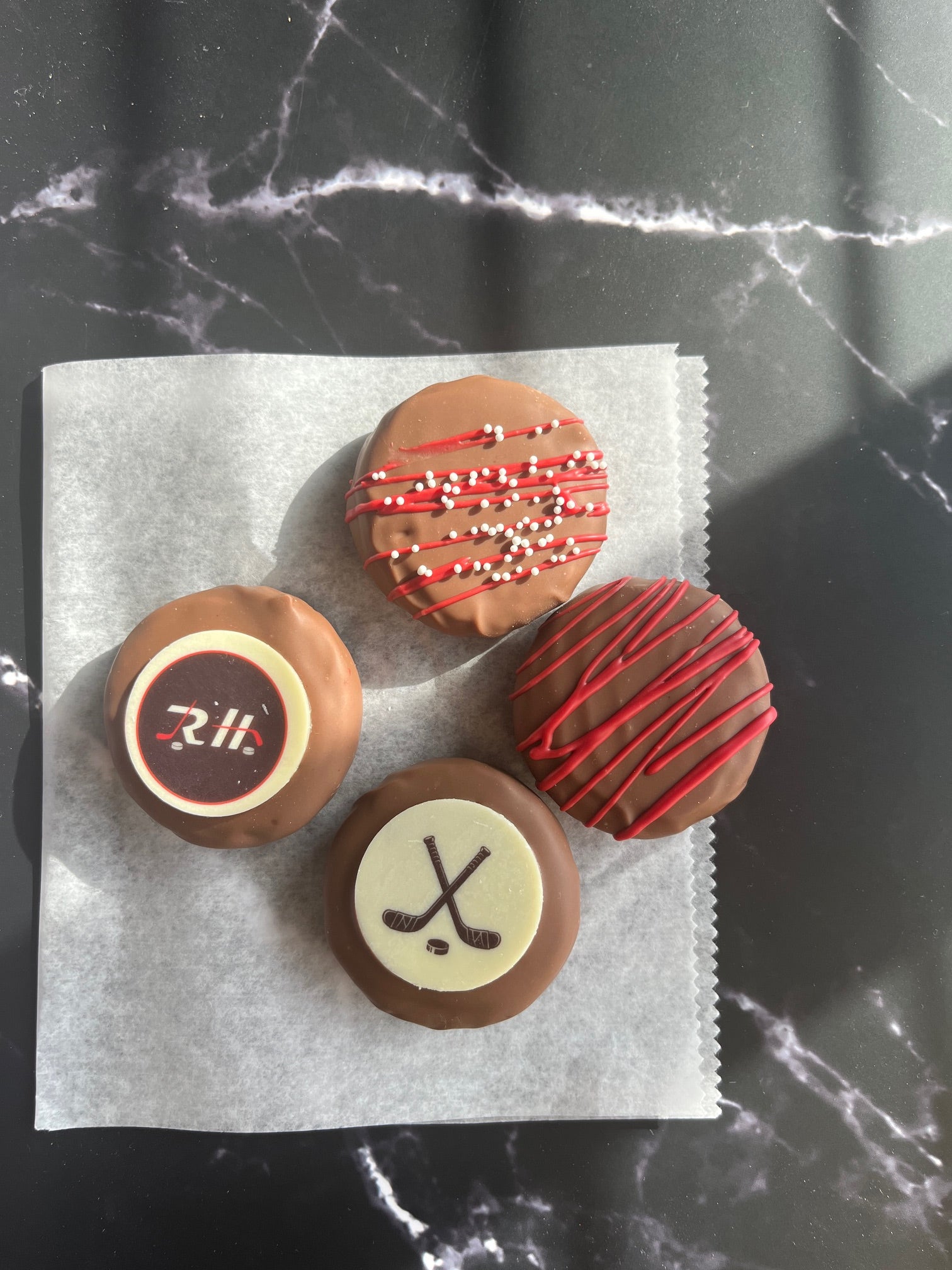 Four chocolate covered Oreos two with custom logo chocolate coins and two with color matched chocolate drizzle.